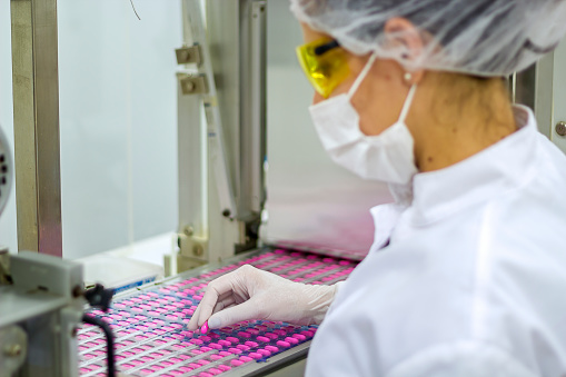 An employee oversees the packaging of the medical pills. Pharmaceutical technolgist wearing protective clothing.