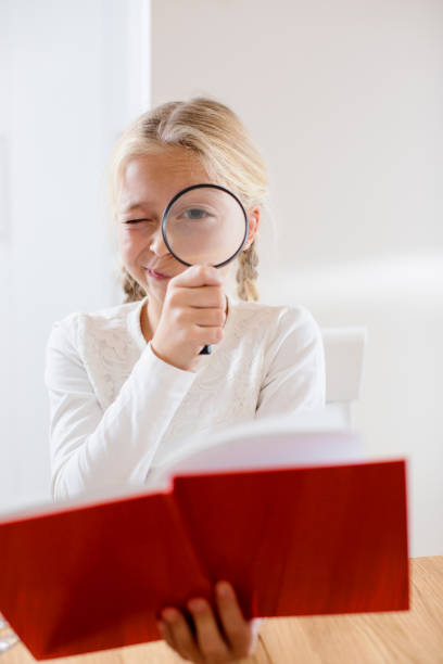 istock Blond school girl reading book through spyglass 670577868