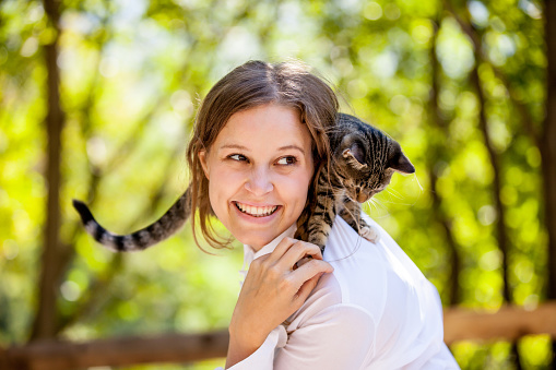 Beautiful young woman enjoying with her cat on shoulder.
