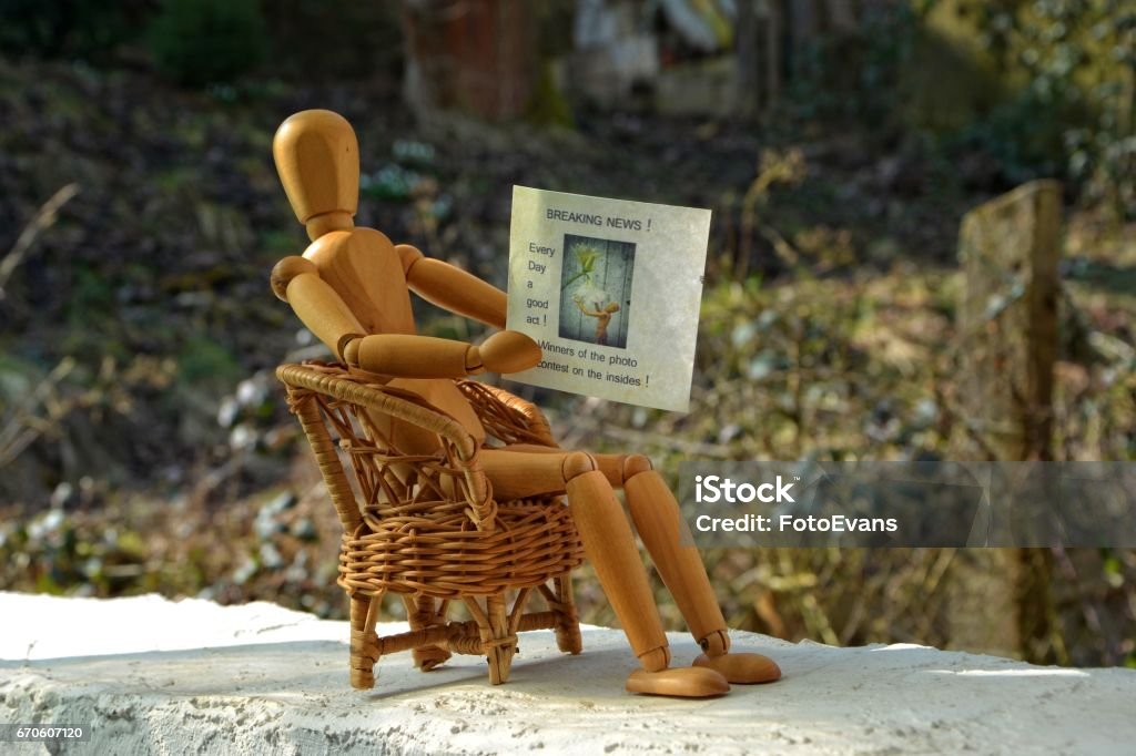 Wooden figure sitting on  chair and reading newspaper Wooden figure sitting on patio chair and reading newspaper Brown Stock Photo