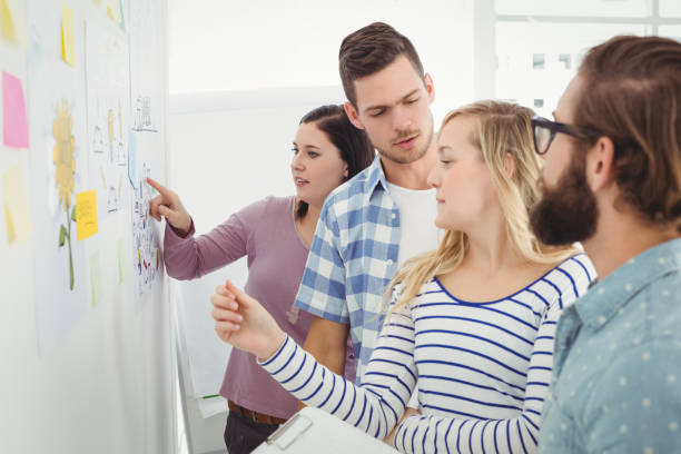 istock Business people talking while standing at wall with sticky notes and drawings 670625854