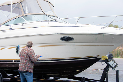 Caucasian man washing boat hull with long handle brush