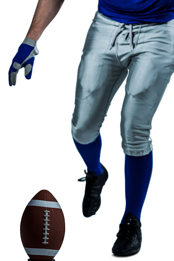 Low section of American football player kicking ball over white background