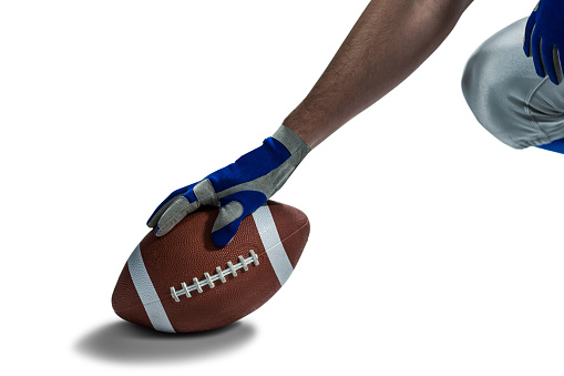 Cropped image of American football player placing ball against white background
