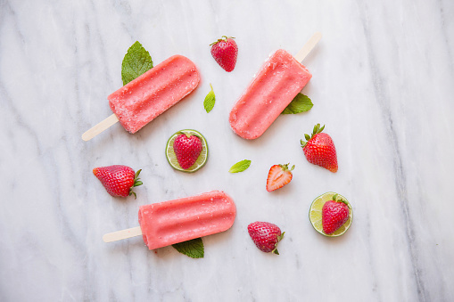 Three Red popsicles with strawberries and limes on a piece of marble with leaves