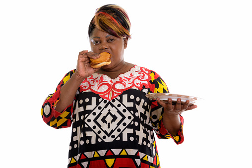 Studio shot of overweight black African woman eating burger while holding white plate horizontal shot