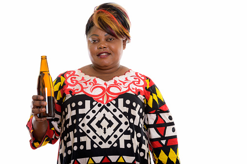 Studio shot of happy overweight black African woman smiling while holding bottle of beer horizontal shot