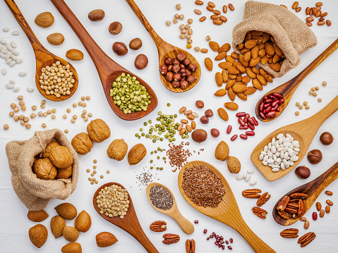 Various legumes and different kinds of nuts in spoons. Walnuts kernels ,hazelnuts, almond ,brown pinto ,soy beans ,flax seeds ,chia ,red kidney beans and pecan set up on white wooden table.