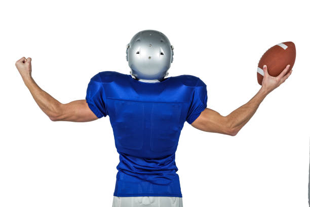 American football player flexing muscles while holding ball Rear view of American football player flexing muscles while holding ball against white background american football player studio stock pictures, royalty-free photos & images