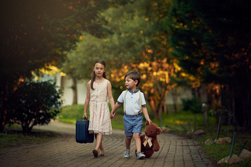 Shot of a little girl and her brother walking while carrying suitcases and toys