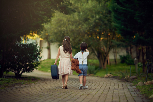 Shot of a little girl and her brother walking away while carrying suitcases and toys
