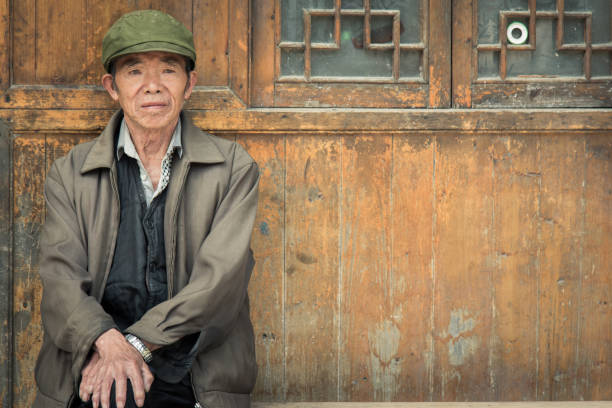 Chinese Senior Man sitting on bench in front of his home in Zhaoxing China Chinese senior man sitting on bench in front of his home with a wooden facade in a rural village. Chinese Real People Portrait. Zhaoxing, Guizhou, China mao original stock pictures, royalty-free photos & images