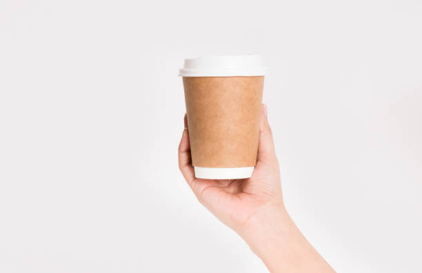 istock Hand holding white empty paper coffee cup with a brown plastic cap isolated on a white background 670692004