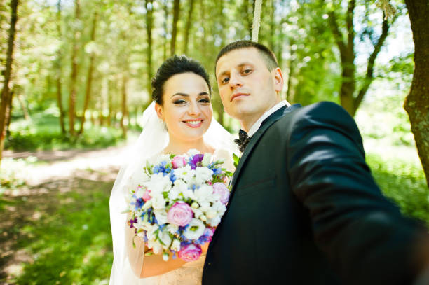 istock Gorgeus wedding couple on green sunny forest. Groom doing selfie 670696486