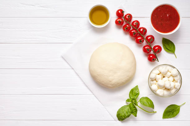 istock Raw pizza dough with ingredients: mozzarella, tomatoes sauce, basil, olive oil, cheese, spices. Italian margherita on wooden table. Italian pizza margarita 670701918