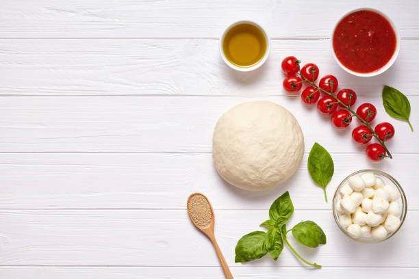 istock Raw pizza dough with baking ingredients: mozzarella cheese, tomatoes sauce, basil, olive oil, cheese, spices. Italian margherita on wooden table. Italian pizza margarita 670701940