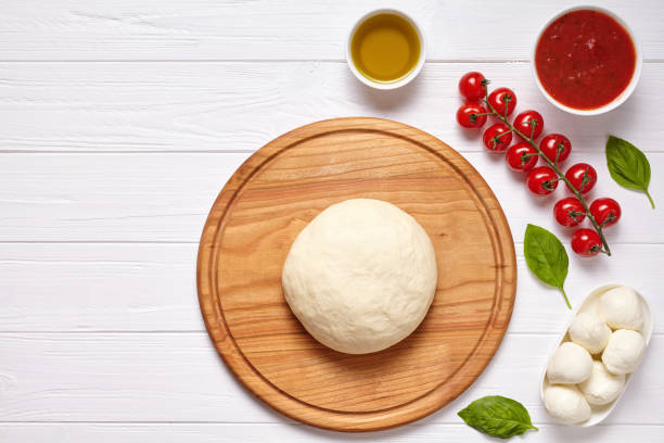 istock Raw pizza dough with baking ingredients on cutting board: dough, mozzarella, tomatoes sauce, basil, olive oil, cheese, spices. Italian margherita on wooden table. Italian pizza margarita 670701980