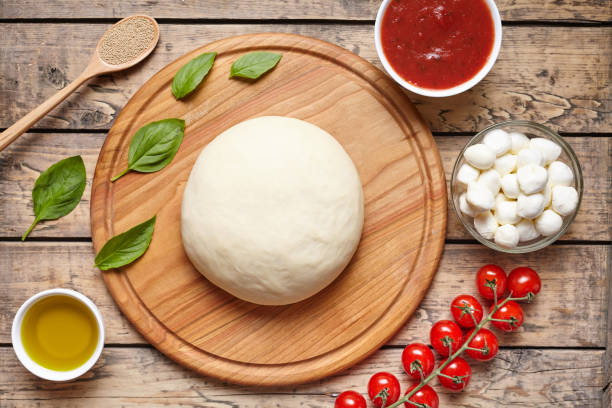 Pizza cooking ingredients on cutting board. Dough, mozzarella, tomatoes, basil, olive oil, spices. Work with the dough. Top view. Flat lay. Traditional italian pizza margherita. stock photo