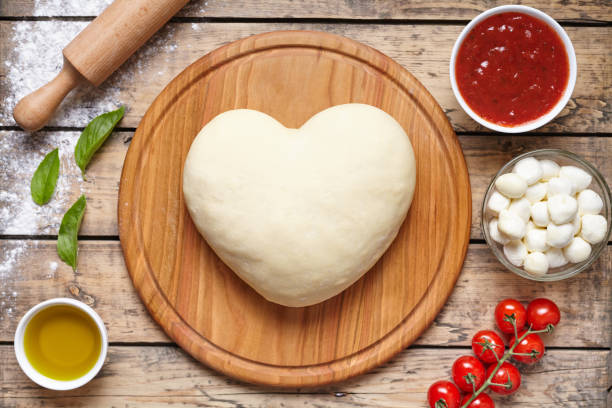 istock Heart shaped pizza cooking ingredients. Dough, mozzarella, tomatoes, basil, olive oil, spices. Work with the dough. Top view. Flat lay. Traditional italian pizza margherita. 670702096