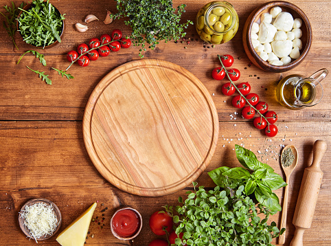 Cutting wooden board with traditional pizza preparation ingridients: mozzarella, tomatoes sauce, basil, olive oil, cheese, spices.