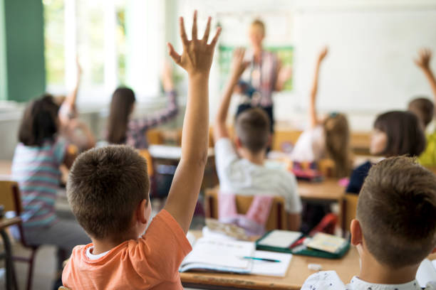 vista posteriore dello scolaro che alza la mano per rispondere alla domanda. - child classroom education school foto e immagini stock