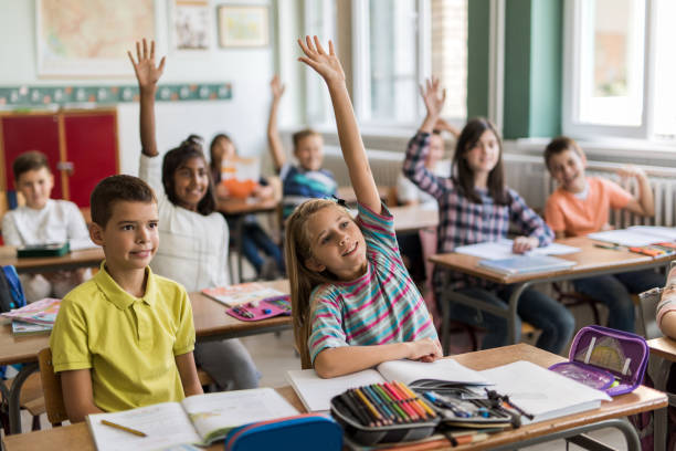 istock Smiling school children with arms raised in the classroom. 670713794