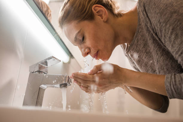 Below view of a woman washing her face in the bathroom. Low angle view of young woman washing her face in her bathroom. woman washing face stock pictures, royalty-free photos & images