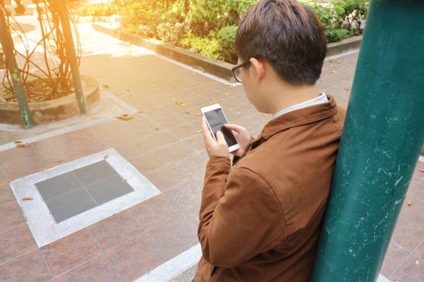 istock Handsome young business man looking mobile phone in his hand while leaning a pole with sunshine effect at outdoor. 670736188