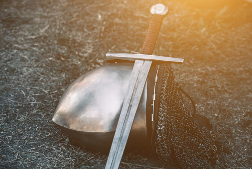 Knight's helmet and shiny metal lying on the ground, it put an old steel sword with leather handle.