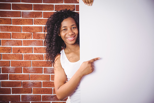 Smiling woman pointing to white board on red brick background