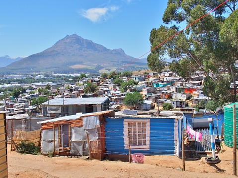 Western Cape, South Africa - November 9, 2016: Informal settlement - Enkanini with mountain and blue sky on the outskirts of Stellenbosch, Western Cape province, South Africa. Many shacks in Enkanini have solar panels for access to electricity.