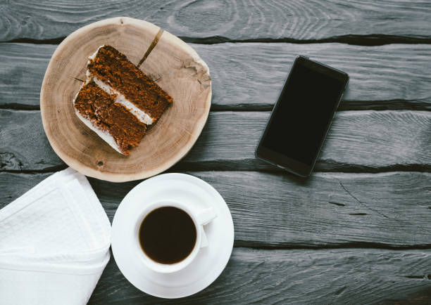 pezzo di torta di biscotti fatta in casa e caffè nero su un tavolo di legno nero. smartphone su un tavolo con pasto. deliziosa colazione di una persona impegnata. - coffee muffin pastry blueberry muffin foto e immagini stock