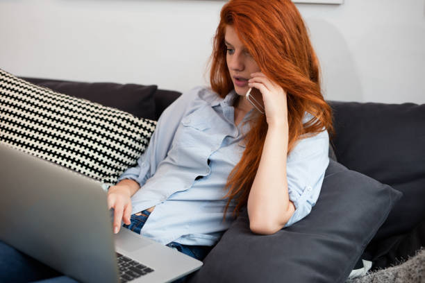 istock Sexy redhead relaxing on the couch with computer in her lap 670793382