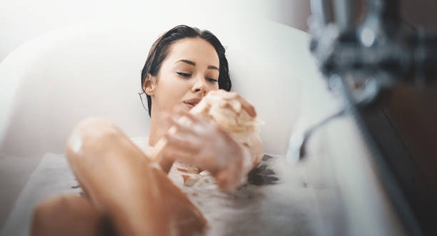 Relaxing bath. Closeup of attractive mid 20's woman taking a long bath in a bathtub. She's slowly scrubbing off with a bath sponge and not planning to get out some time soon. shower gel stock pictures, royalty-free photos & images