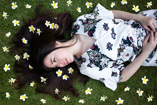 Low angle view of a beautiful young woman lying down in the grass, and smelling the white flowers. Nature, taking care concept