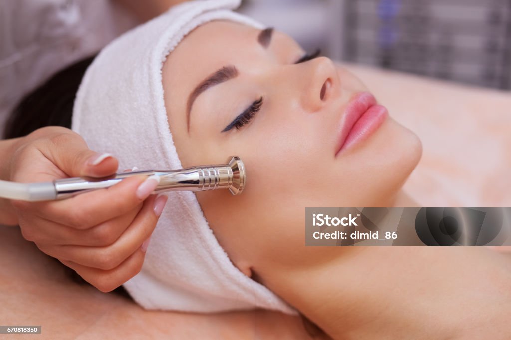 doctor-cosmetologist makes the procedure Microdermabrasion of the facial skin of a beautiful, young woman in a beauty salon The doctor-cosmetologist makes the procedure Microdermabrasion of the facial skin of a beautiful, young woman in a beauty salon.Cosmetology and professional skin care. Healthcare And Medicine Stock Photo