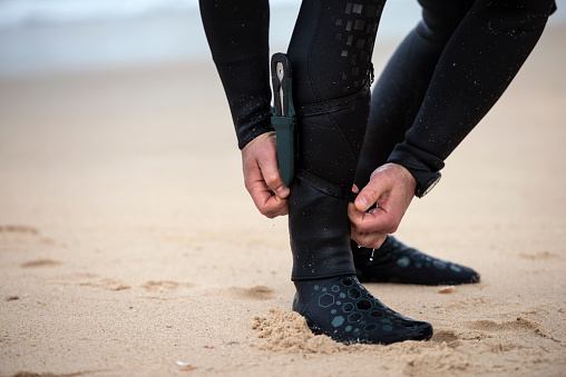Diver adjusting his wetsuit's ankle panels so that it fits perfectly with dive knife.