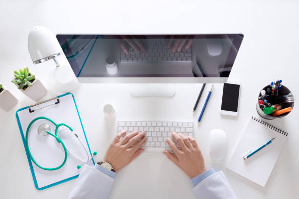 Top view of doctor sitting at the desk and using computer, unrecognizable person.