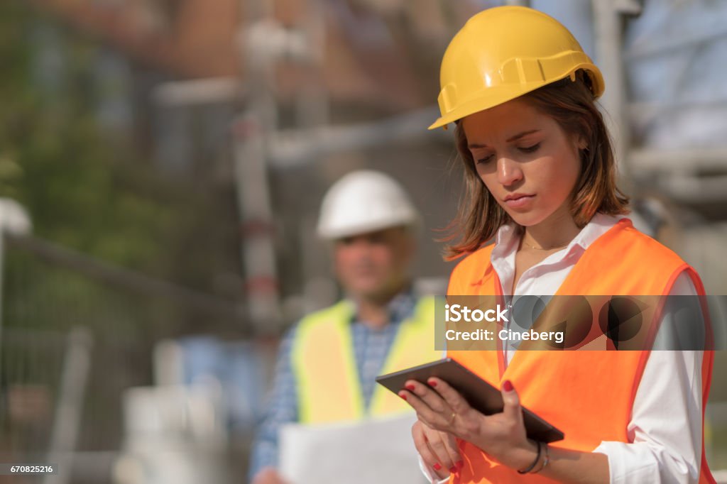 Pensive, thoughtful young civil engineer working with her touchless tablet on construction site Construction Site Stock Photo