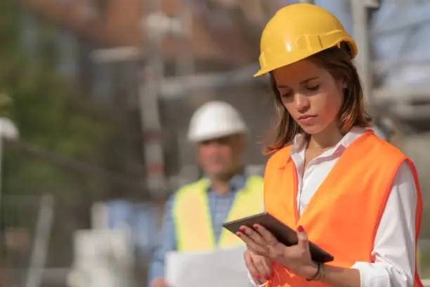 Pensive, thoughtful young civil engineer working with her touchless tablet on construction site