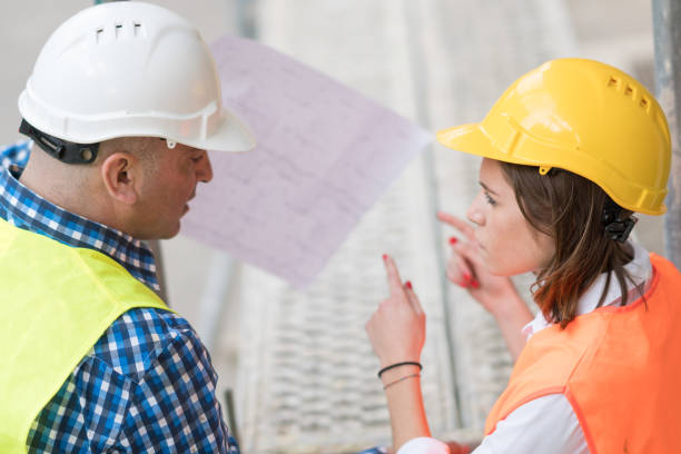 istock Back turned technician and architect at construction site reviewing office blueprints and technical drawings 670825236