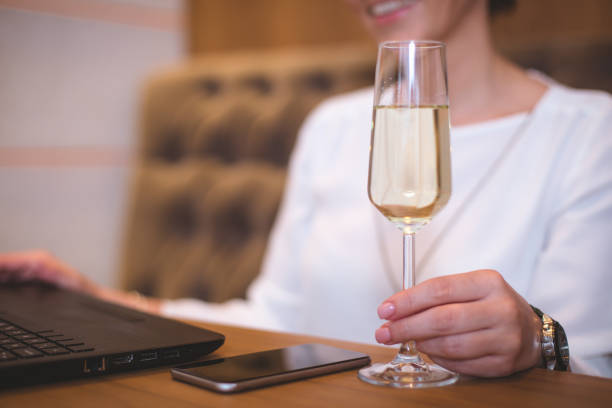 istock Elegant female holding champagne glass while using laptop at the restaurant 670829040