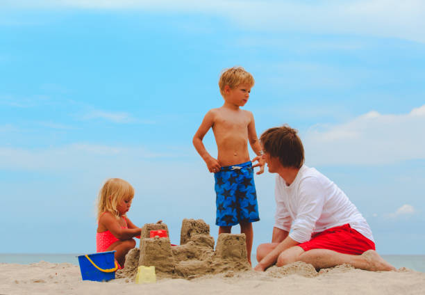 istock father with son and daughter building castle on beach 670831356