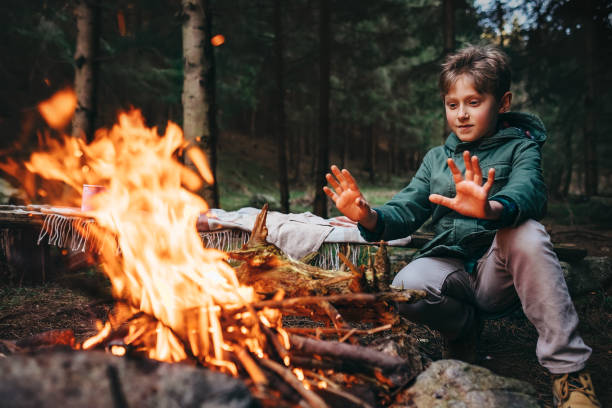 Boy warms his hands near campfire in forest Boy warms his hands near campfire in forest warms stock pictures, royalty-free photos & images