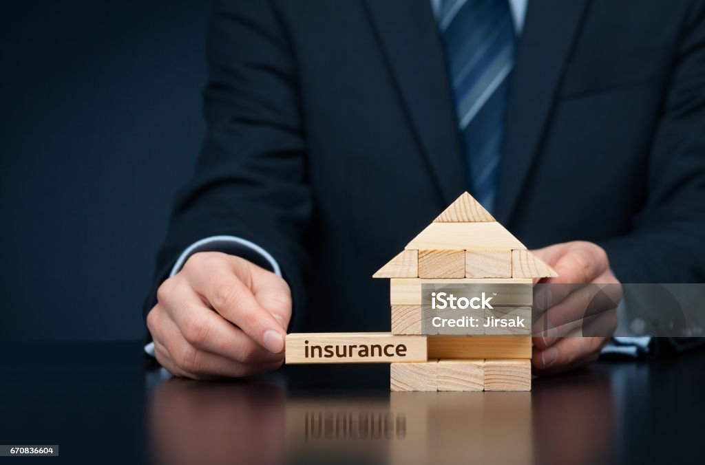 Property (family house) insurance protection concept Property (family house) insurance protection concept. Insurance agent complete wooden model of the house with last piece with text insurance. Adult Stock Photo