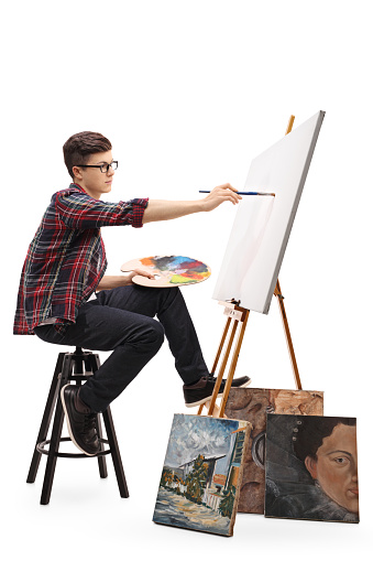 Profile shot of a teenage painter painting on a canvas with a paintbrush isolated on white background