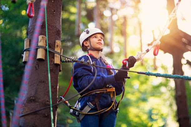 Happy, confident teenage girl having fun on canopy tour. The girl is staning high up and detaching carabiner from zip line.\n