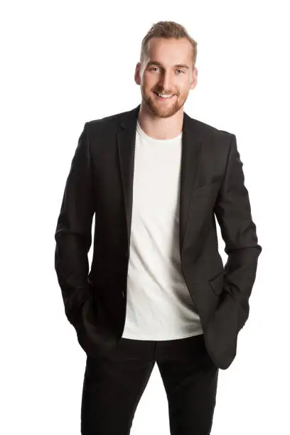 Handsome blonde man standing in front of a white background wearing a black blazer. Smiling looking at camera.