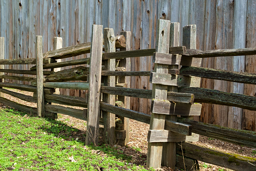 Sliding gate in rustic split-rail wooden fence in sunshine with tall wood fence in background at Fort Nisqually in Tacoma, Washington