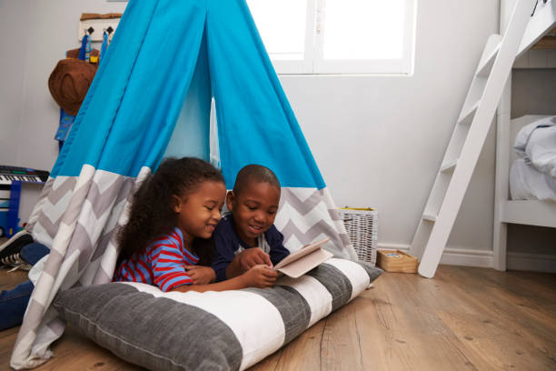 zwei kinder im zelt im spielzimmer mit digital-tablette liegen - tipi bett stock-fotos und bilder